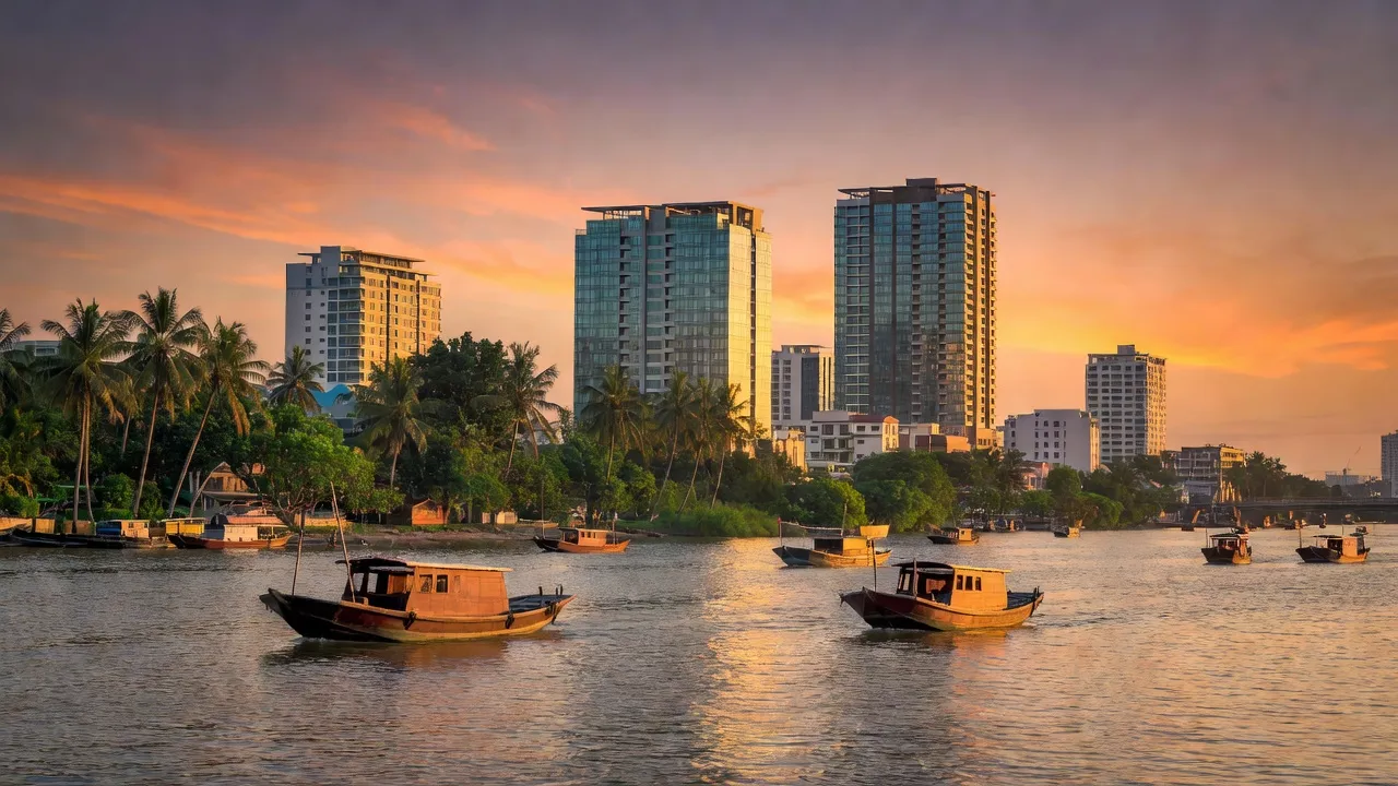 Thành phố Cần Thơ với cây xanh, thuyền truyền thống và ánh hoàng hôn phản chiếu trên sông.